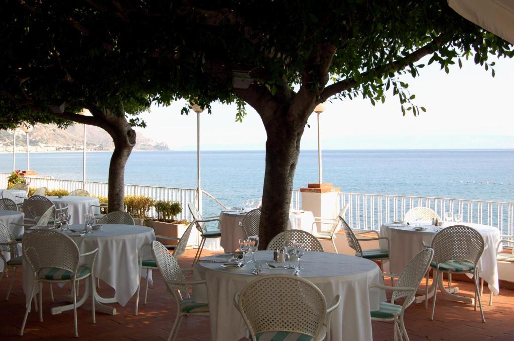 a restaurant with white tables and chairs and the ocean at Hotel Lido Mediterranee in Taormina