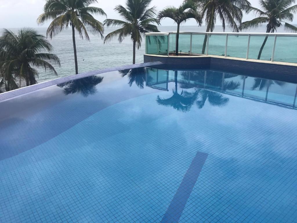 una gran piscina con palmeras y el océano en LUXUOSO APARTAMENTO COSTA ESPANHA Barra SALVADOR, en Salvador