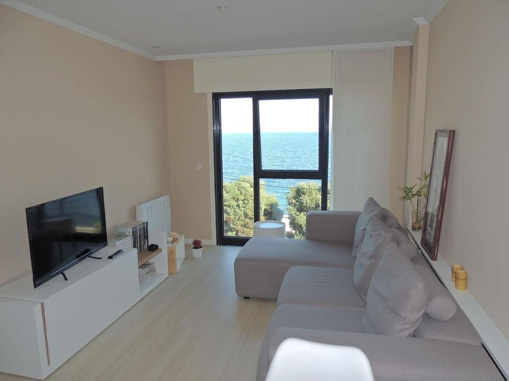 een woonkamer met een witte bank en een televisie bij Apartamento romántico con el mar a tus pies in Ribeira