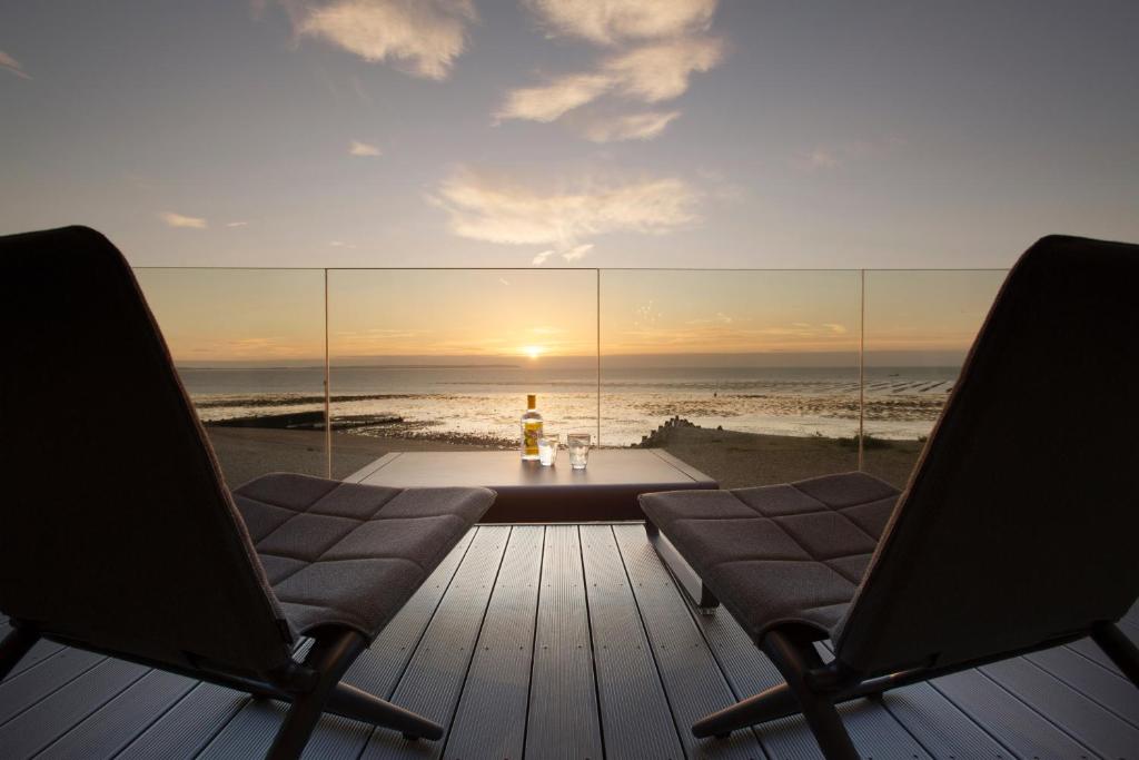 two chairs on a deck with a table and the ocean at Sea Sunset Cottage in Whitstable