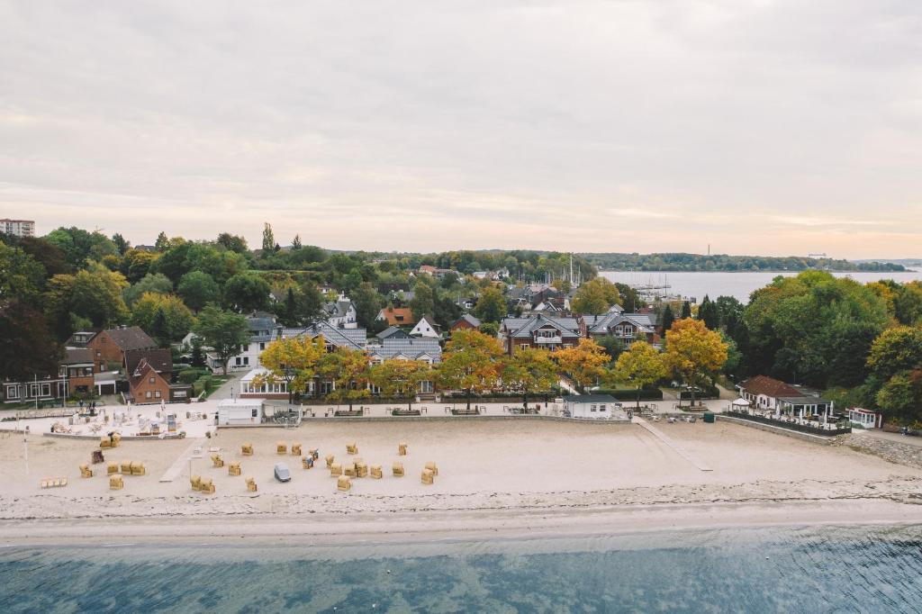 eine Luftansicht auf einen Strand mit Stühlen und Eigentumswohnungen in der Unterkunft StrandHotel Seeblick, Ostseebad Heikendorf in Heikendorf