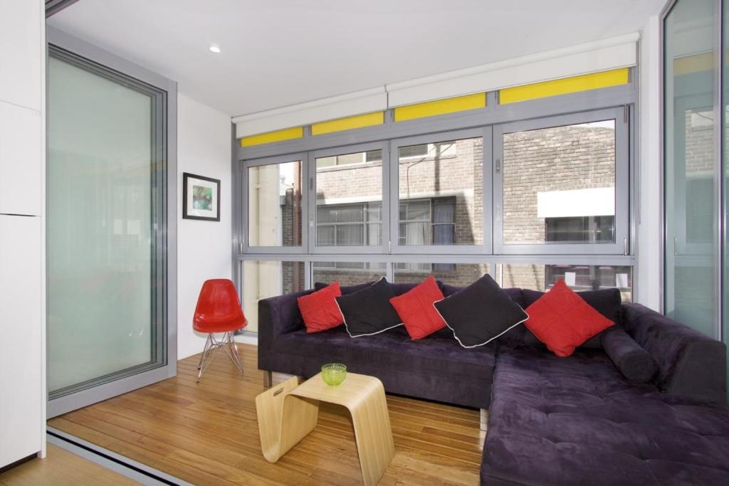 uma sala de estar com um sofá preto e almofadas vermelhas em Little New York on Riley - Executive 1BR Darlinghurst Apartment with New York Laneway Feel em Sydney
