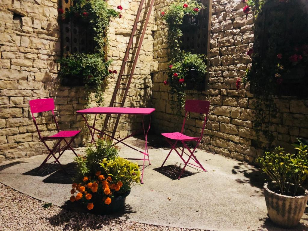 une table et des chaises roses dans une cour fleurie dans l'établissement Maison d'hôtes La Colombelle, à Colombé-le-Sec