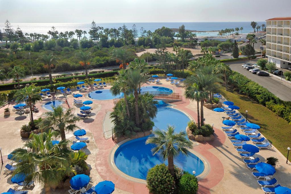an overhead view of a resort pool with blue umbrellas and palm trees at Nissiana Hotel & Bungalows in Ayia Napa