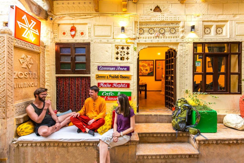 tre persone sedute su una panchina di fronte a un edificio di Zostel Jaisalmer a Jaisalmer