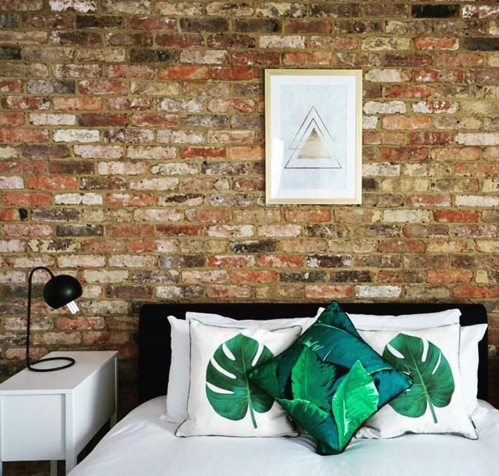 a bedroom with a brick wall and a bed with green pillows at N5 Townhouse, Brighton Sleeps 20 in Brighton & Hove