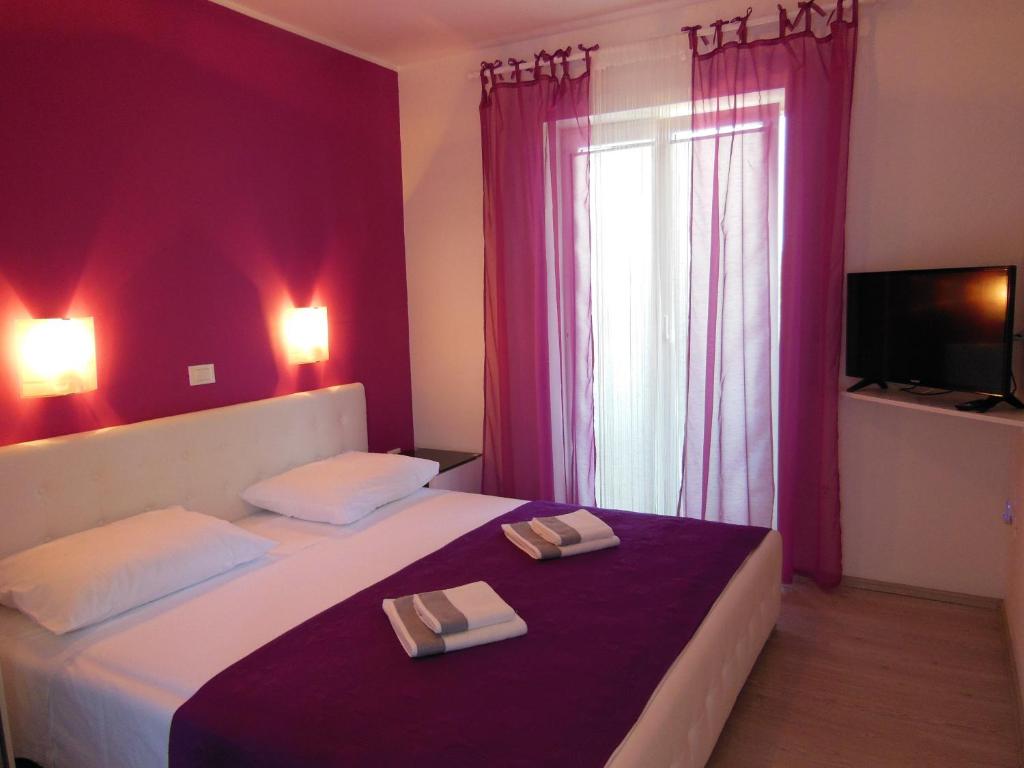 - une chambre avec 2 lits aux murs violets et une fenêtre dans l'établissement Villa Kamelija, à Fažana
