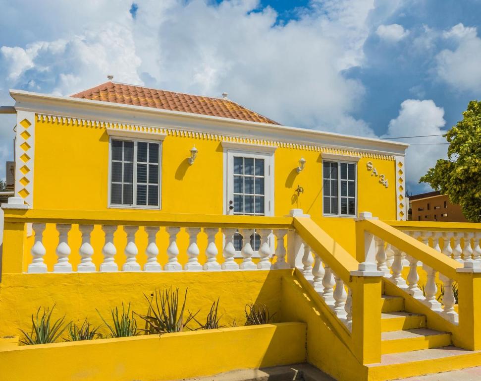 a yellow house with a white fence and stairs at Old Aloe House in Savaneta