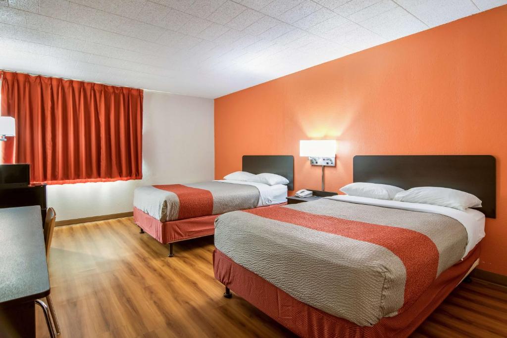 Motel 6-New Stanton, PA في نيو ستانتون: سريرين في غرفة الفندق بجدران برتقالية