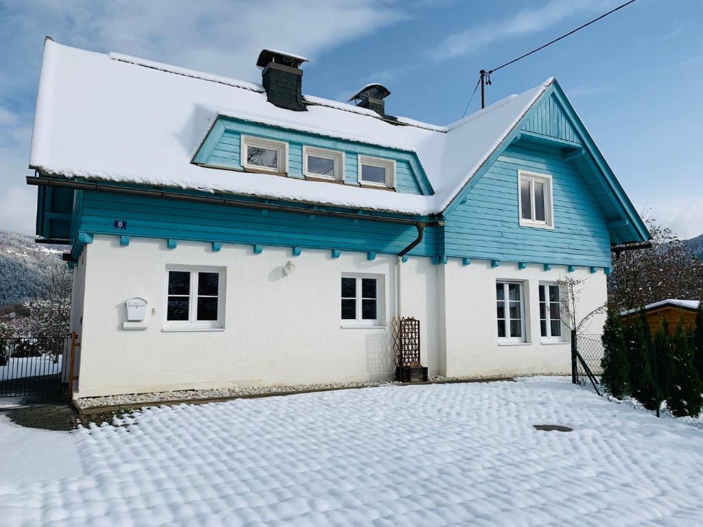 a blue and white house with a snow covered driveway at Blaues Haus Ferienwohnung Bodensdorf Ossiacher See Gerlitzen Alpe in Bodensdorf