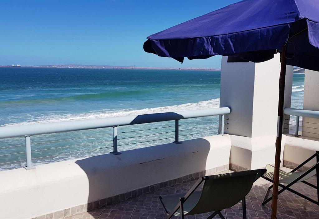 a balcony with an umbrella and chairs and the ocean at On the Beach 1 in Langebaan