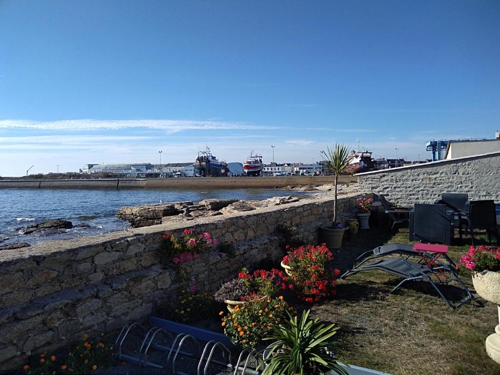 a stone wall with chairs and flowers next to the water at La Rose des Mers in Tréffiagat
