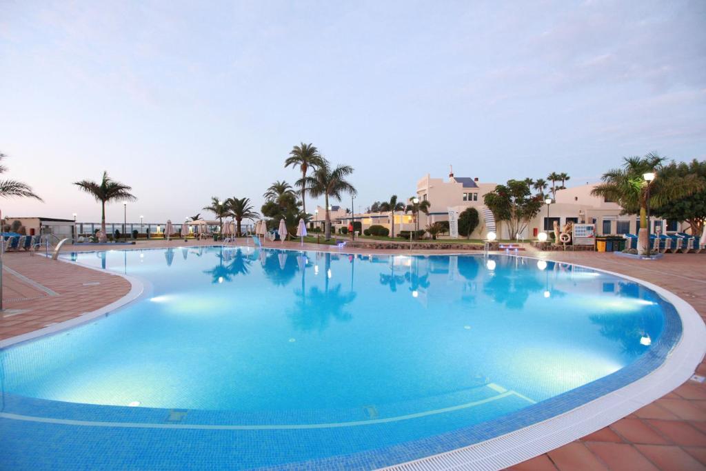 duży błękitny basen z palmami i domami w obiekcie Grupotel Playa Feliz w mieście San Agustin