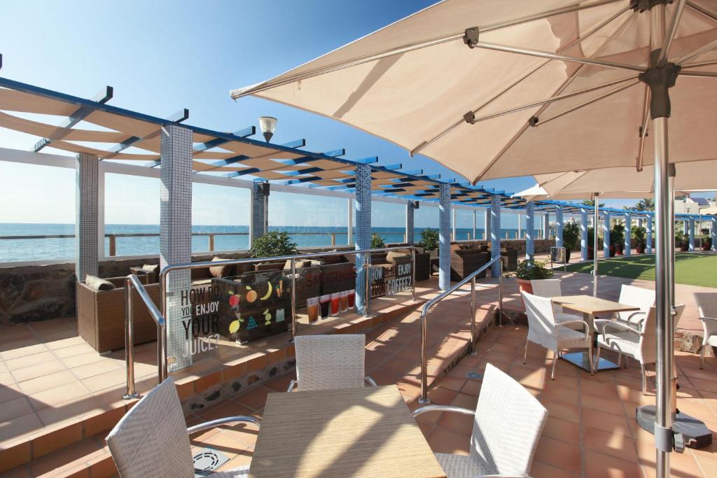 taras ze stołami, krzesłami i parasolem w obiekcie Grupotel Playa Feliz w mieście San Agustin