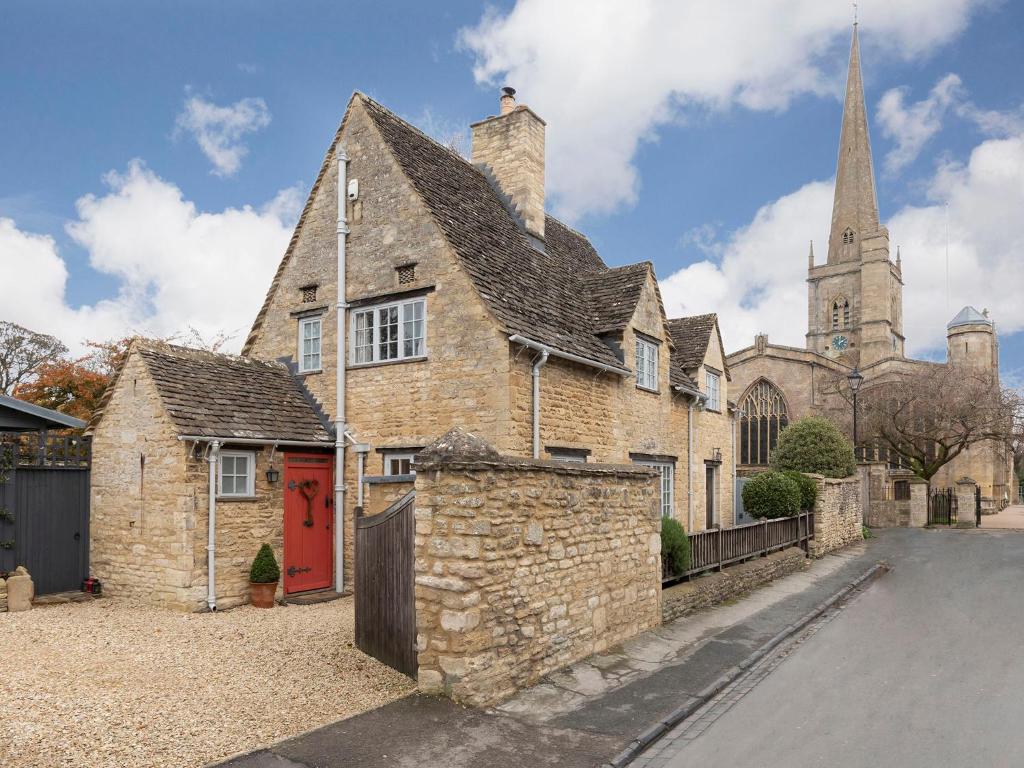 an old stone house with a red door and a church at Church Cottage in Burford