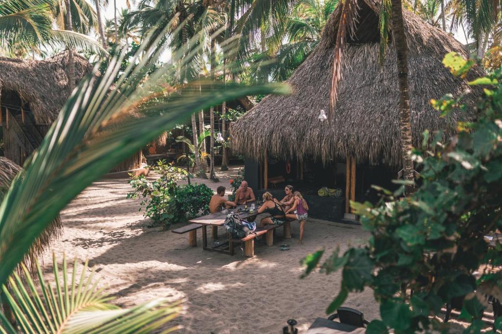 un grupo de personas sentadas en bancos frente a una choza en Los Hermanos Beach Hostal, en Guachaca