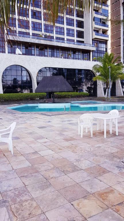 two white chairs and a pool in front of a building at Aconchegante Flat na Orla in Recife