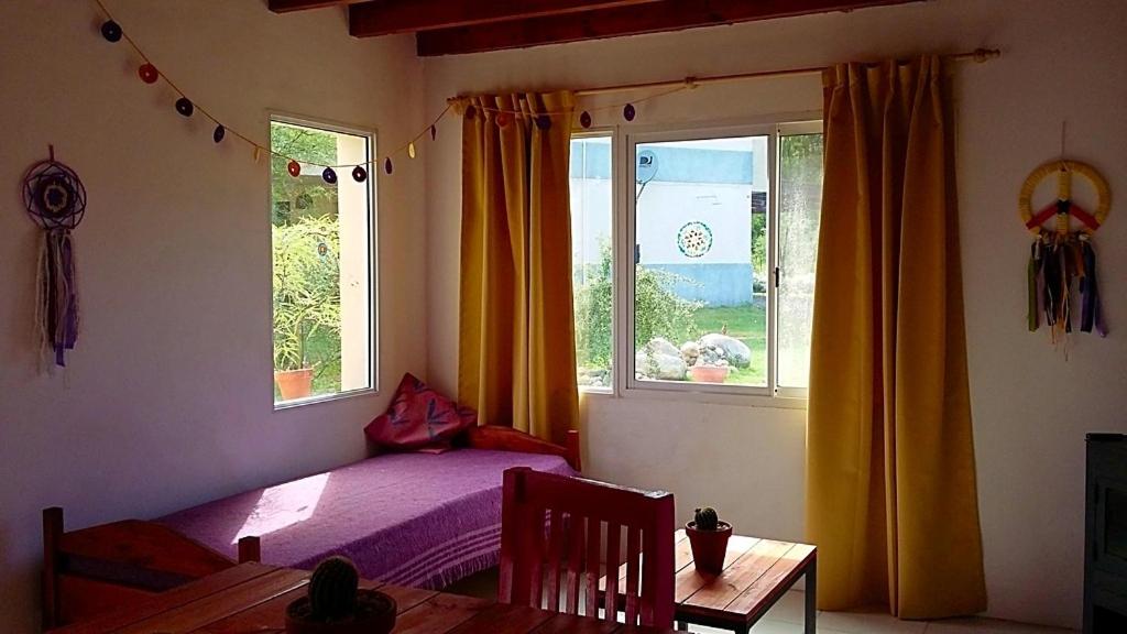 a bedroom with a bed and a table and two windows at Sueño del Champaquí in Villa Las Rosas