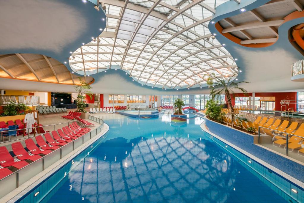 a large swimming pool with red chairs and a ceiling at H2O Hotel-Therme-Resort, für Familien mit Kindern in Bad Waltersdorf