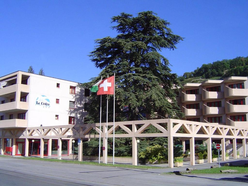 a building with a canadian flag next to a tree at Hotel Le Cedre in Bex