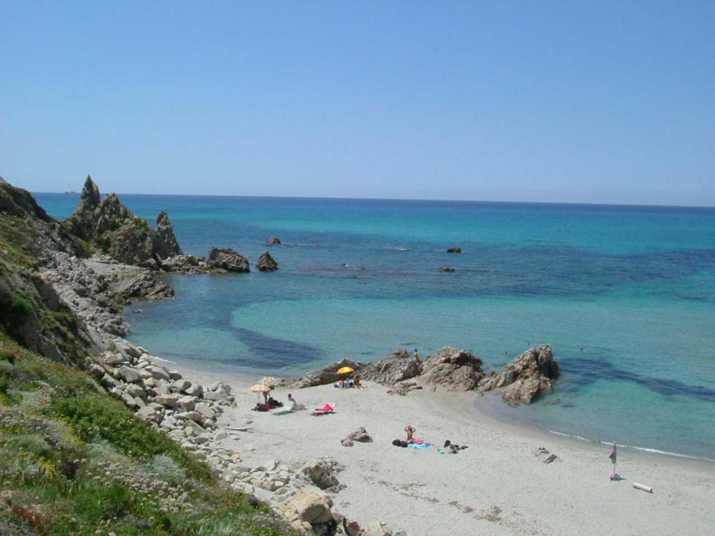 a beach with people laying on the sand and the ocean at Appartamenti Rena Majore in Aglientu