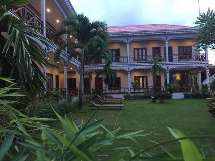a large building with a palm tree in front of it at Mama Leurth Sunset Guesthouse in Don Det