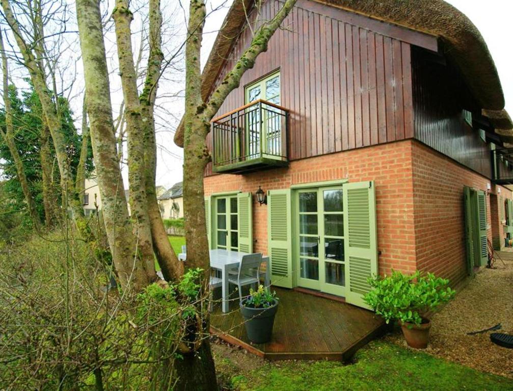 Carp's Rise Cottage في Somerford Keynes: منزل صغير بأبواب خضراء وشرفة