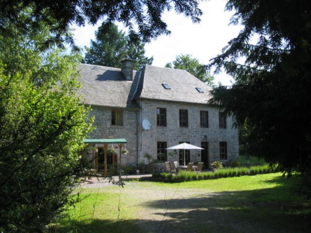 une grande maison en pierre avec un parasol dans la cour dans l'établissement Chambres d'Hôtes Le Pont, à Égletons