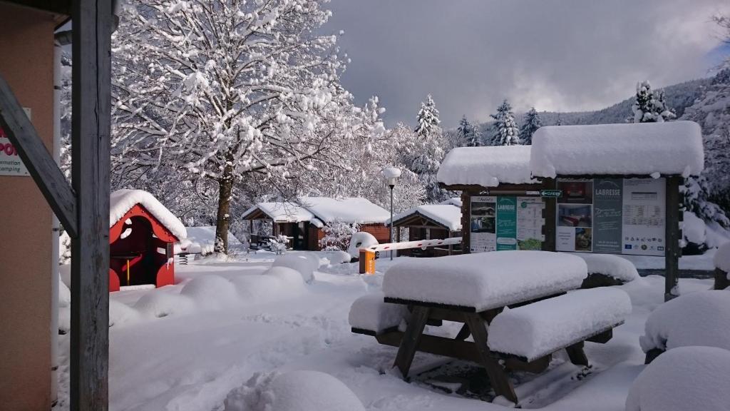 un patio cubierto de nieve con bancos cubiertos de nieve en camping du haut des bluches, en La Bresse