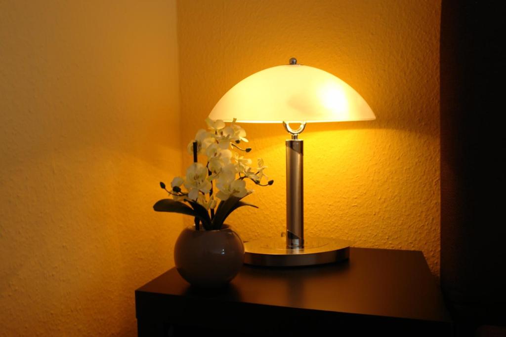 a table with a lamp and a vase with flowers at Pension Zeitlos in Potsdam