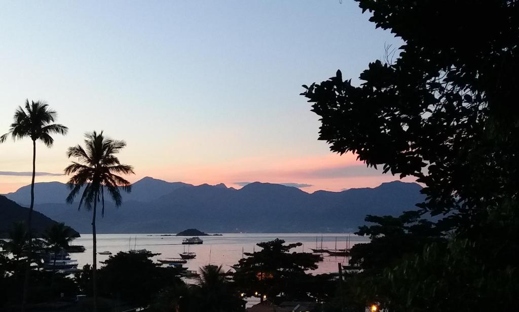 a sunset over the water with palm trees and mountains at Bergamota in Abraão