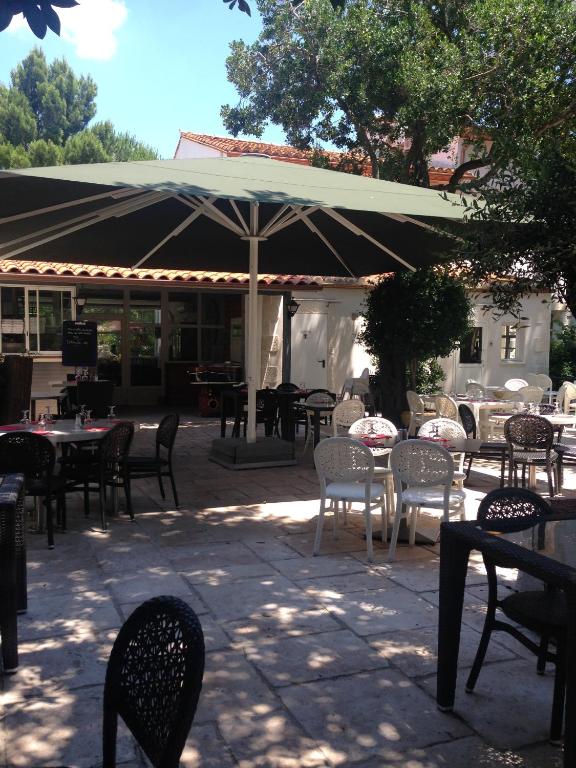un patio avec tables, chaises et un parasol dans l'établissement Le Jardin des Oliviers, à Sigean
