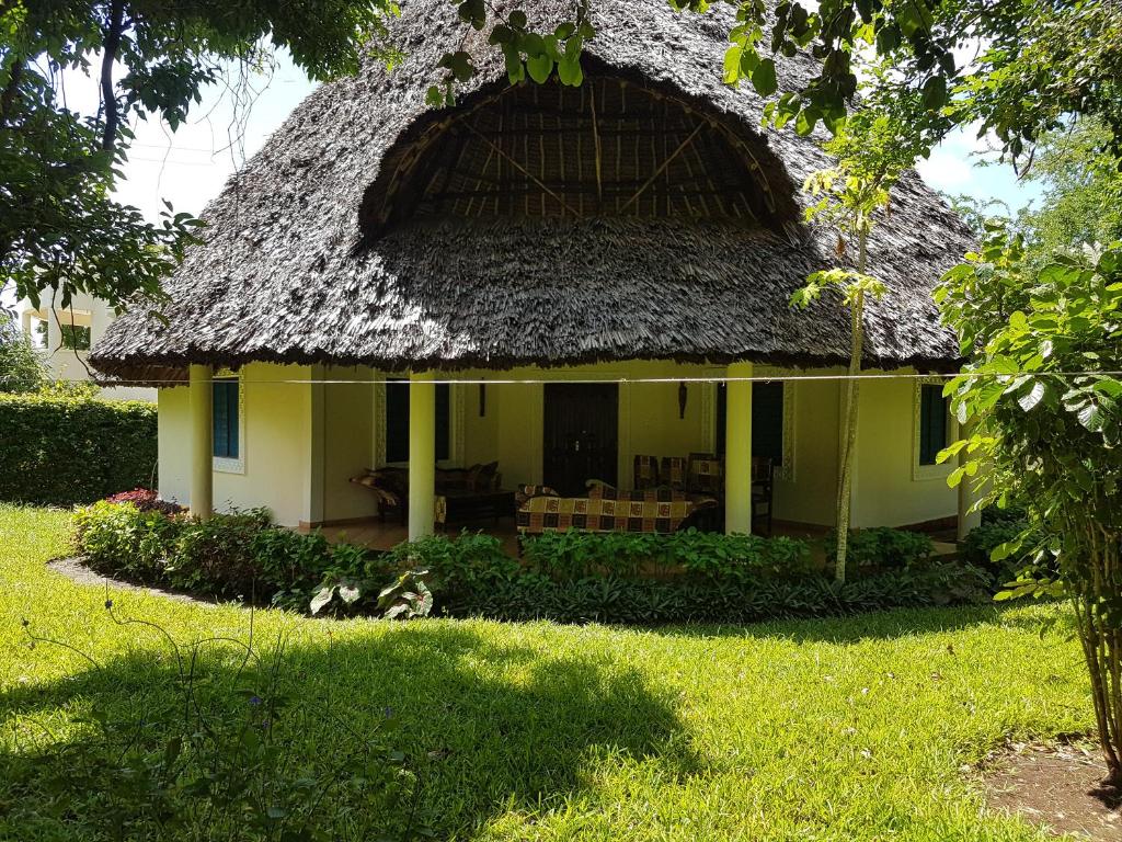 a small yellow house with a thatch roof at Villa LeoMar Diani Beach in Diani Beach