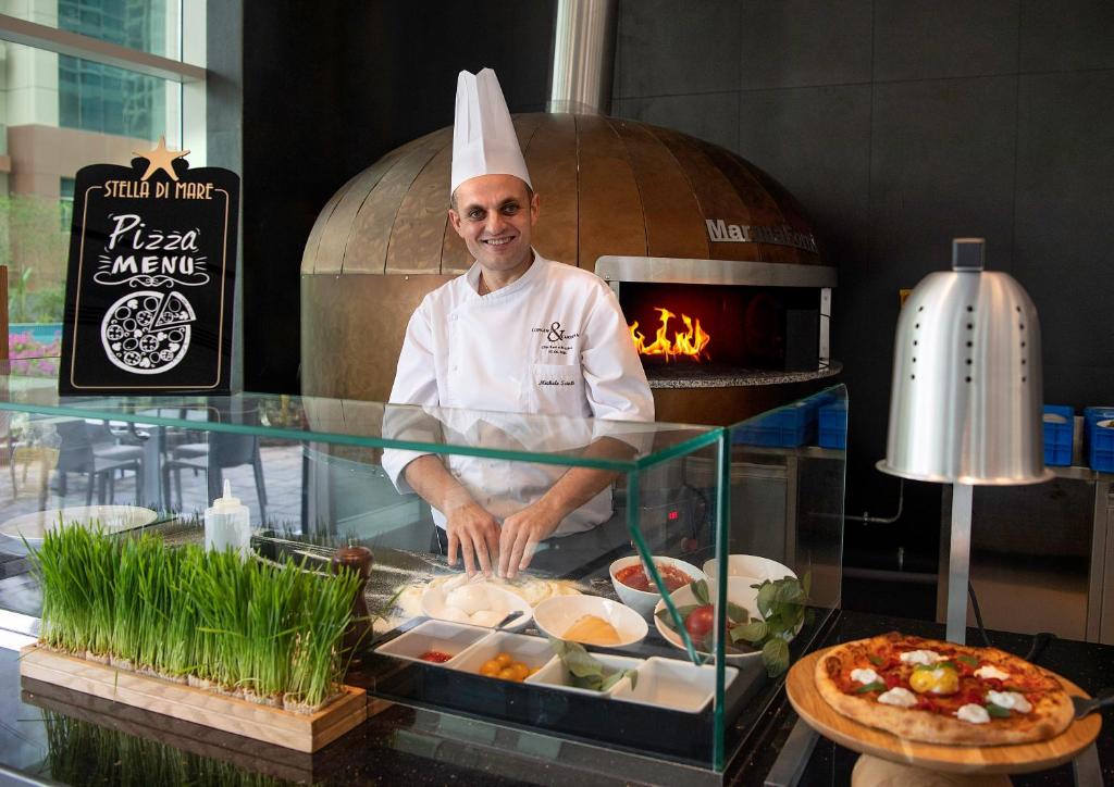 a chef standing in front of a counter with food at Stella Di Mare Dubai Marina Hotel in Dubai