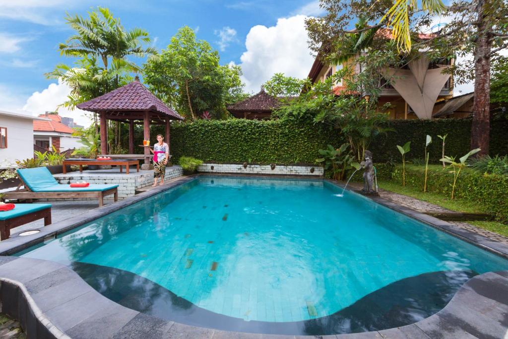 a swimming pool with a woman standing in front of a house at Sayong House in Ubud