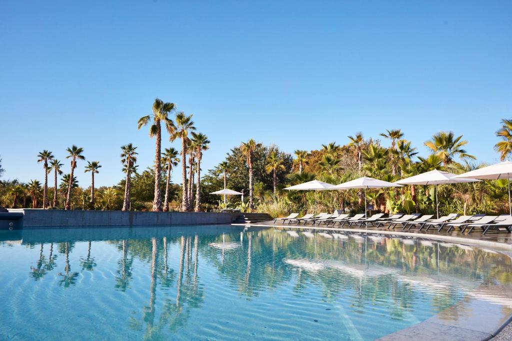 einen Pool mit Stühlen, Sonnenschirmen und Palmen in der Unterkunft Nova Lodges in Grimaud