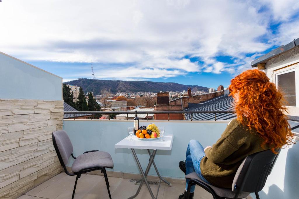 una mujer sentada en una silla en un balcón con una mesa en ANNA en Tiflis
