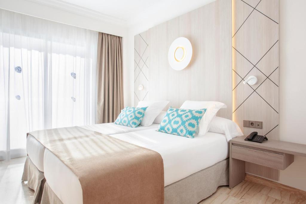 a bedroom with a large white bed with blue pillows at Grupotel Los Príncipes & Spa in Playa de Muro