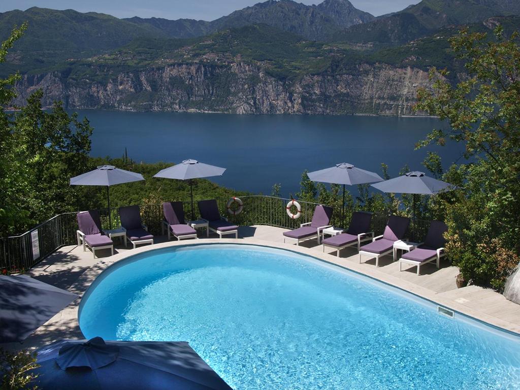 une piscine avec des chaises et des parasols et un lac dans l'établissement Hotel Querceto Wellness & Spa - Garda Lake Collection, à Malcesine