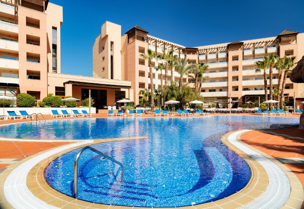 une grande piscine avec des chaises bleues et des bâtiments dans l'établissement H10 Salauris Palace, à Salou