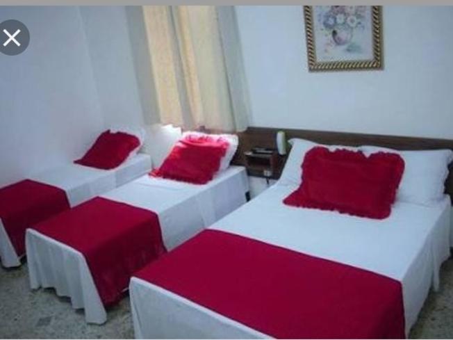 two beds with red pillows in a room at Quartos Uberlandia in Uberlândia