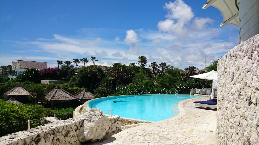 a swimming pool at a resort with a stone wall at Boutique hotel villa Cantik and karma beach club in Uluwatu