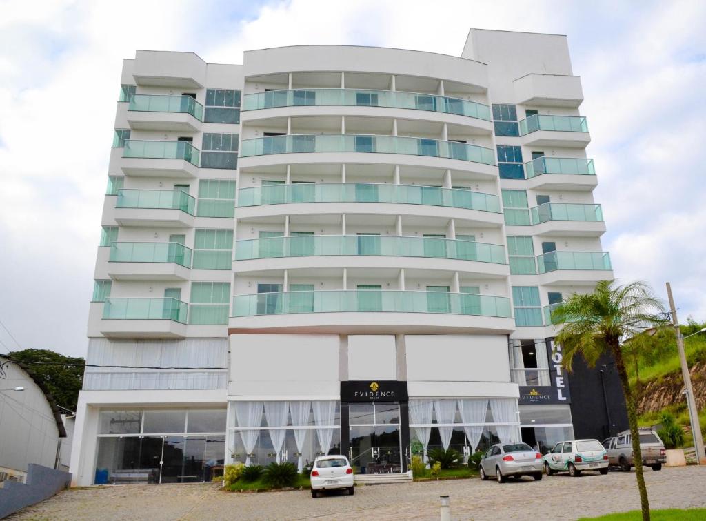 un edificio blanco alto con coches estacionados frente a él en Evidence Hotel, en Sapucaia