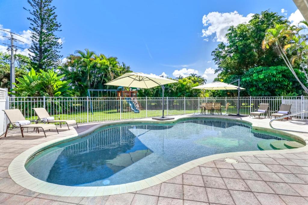 a swimming pool with chairs and umbrellas next to a fence at Comfortably Chic Pool Home Retreat in Naples
