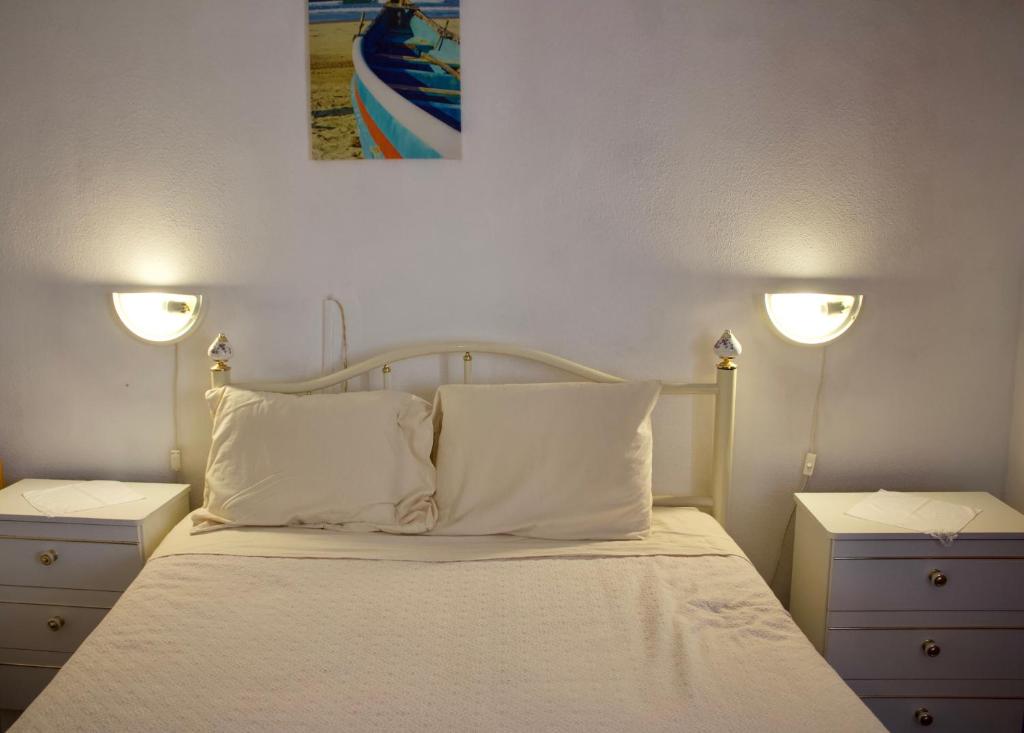 Residencial Tarouca في فانداو: غرفة نوم بسرير وملاءات بيضاء واضاءين