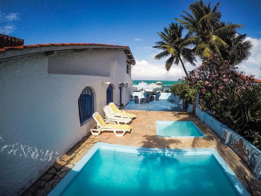 a swimming pool next to a building with a view of the ocean at Pousada Ruínas do Pilar in Itamaracá