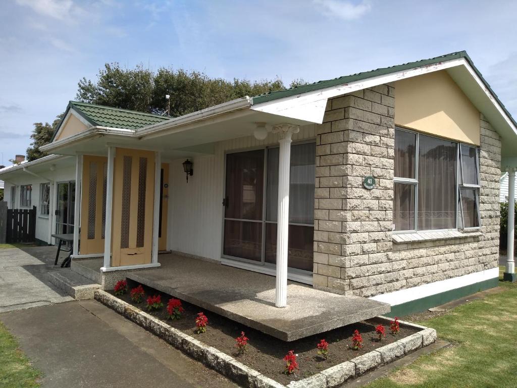 ein kleines Haus mit roten Blumen davor in der Unterkunft Ironsands B&B in Patea