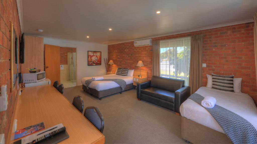 a hotel room with two beds and a desk and a chair at Pevensey Motor Lodge in Echuca
