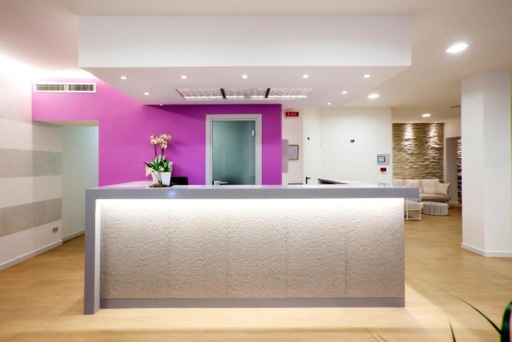 a lobby with a pink wall and a reception counter at Hotel Lux in Caorle