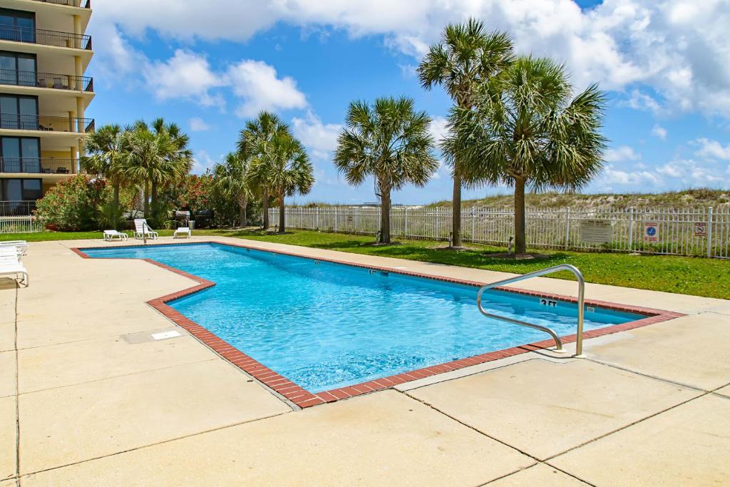 a swimming pool with palm trees and a building at Coastal Haven in Dauphin Island